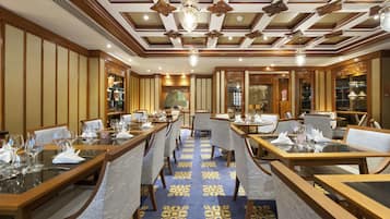 A restaurant with wooden tables and chairs, a patterned carpet, and a decorative ceiling.