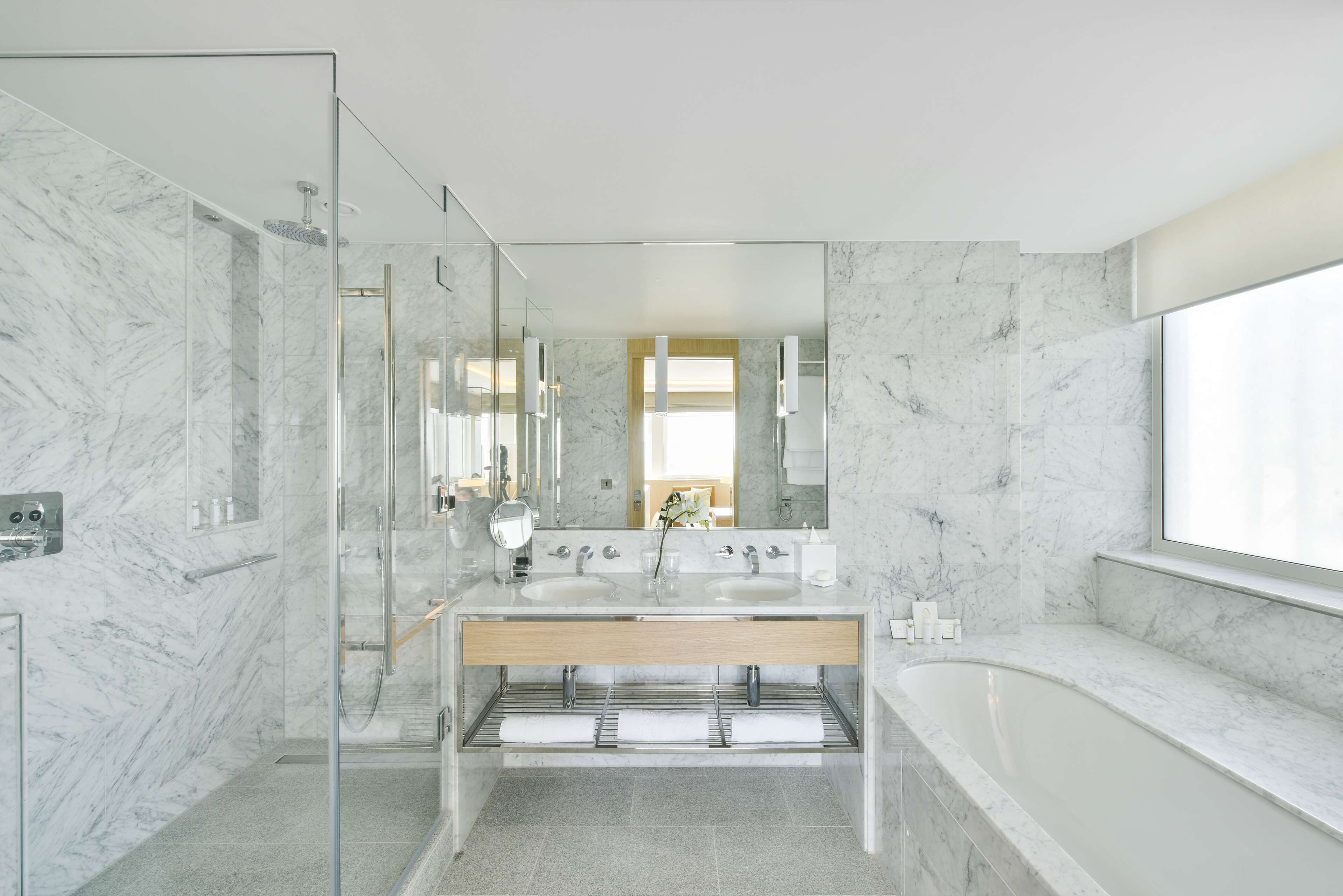 Un baño moderno con paredes de mármol, ducha con cerramiento de vidrio y una bañera grande.