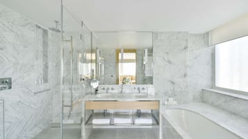 Un baño moderno con paredes de mármol, ducha con cerramiento de vidrio y una bañera grande.