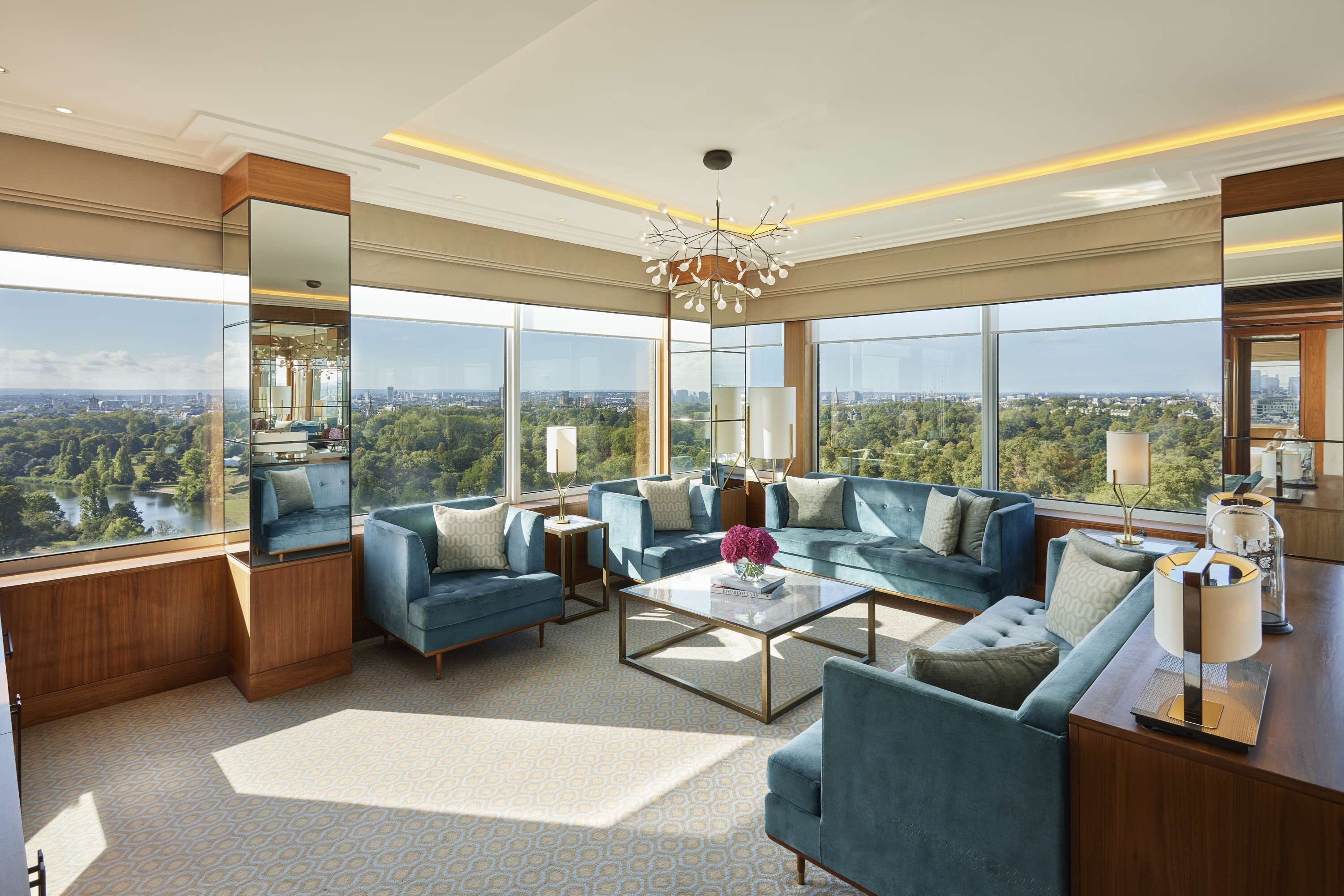 A spacious living room with a large sofa set, a coffee table, and a view of a cityscape through large windows.