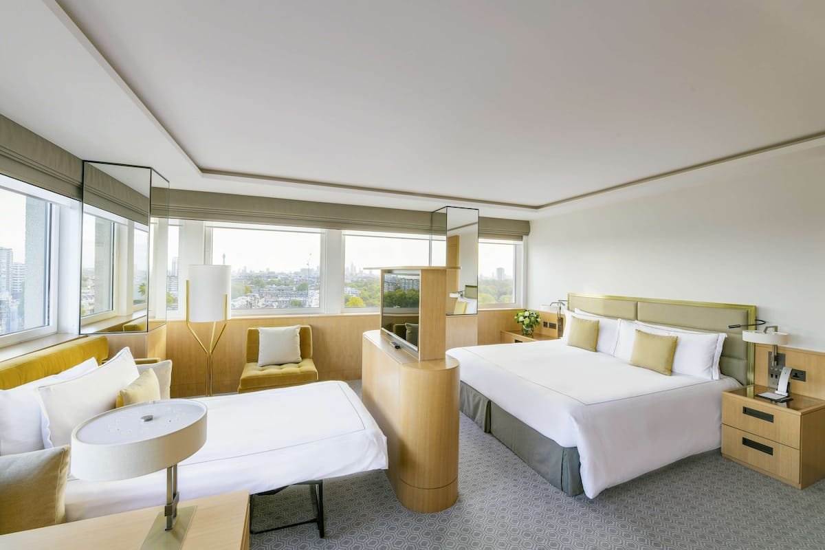 A hotel room with two beds, a sofa, a desk, a mirror, and a view of the city.