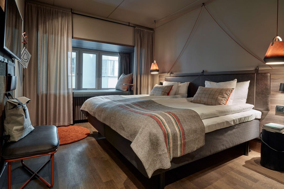 A modern hotel room with a large bed, a desk, and a window with curtains.
