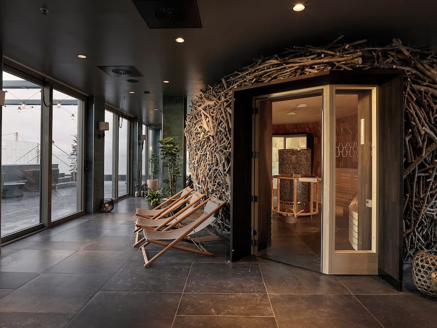 Un interior moderno con entrada de puerta de cristal, un banco de madera y una pared decorada con ramas.