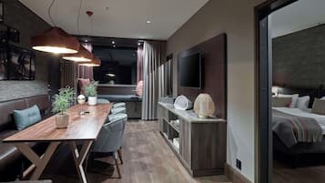 Una sala moderna con una mesa de comedor de madera, sillas tapizadas en gris, un televisor plano grande y una zona de estar acogedora con sofá y cojines.