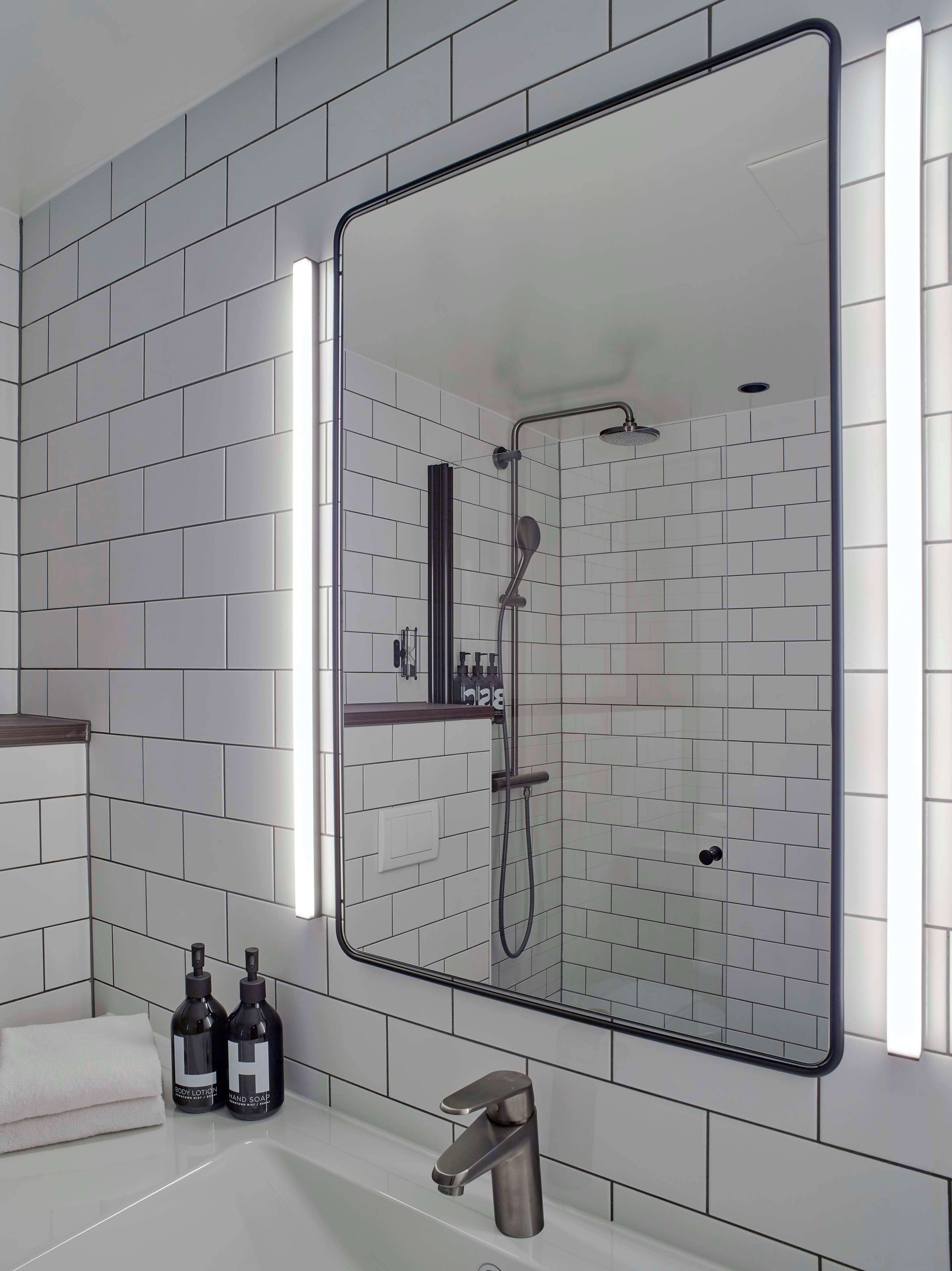 A modern bathroom with a glass-enclosed shower, white tiled walls, and a large mirror.