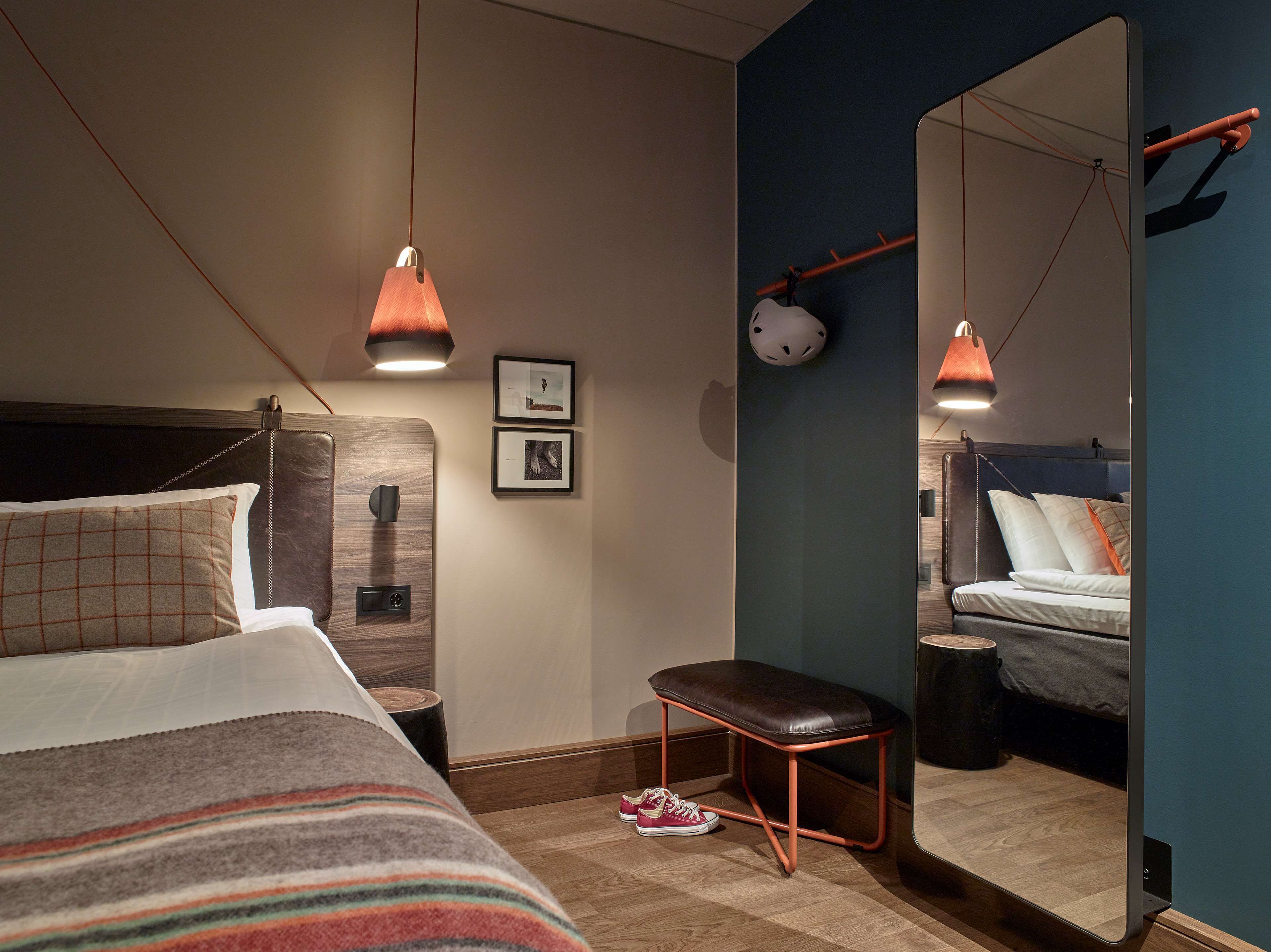 A modern bedroom with a large bed, a bench, a mirror, and two pendant lights.