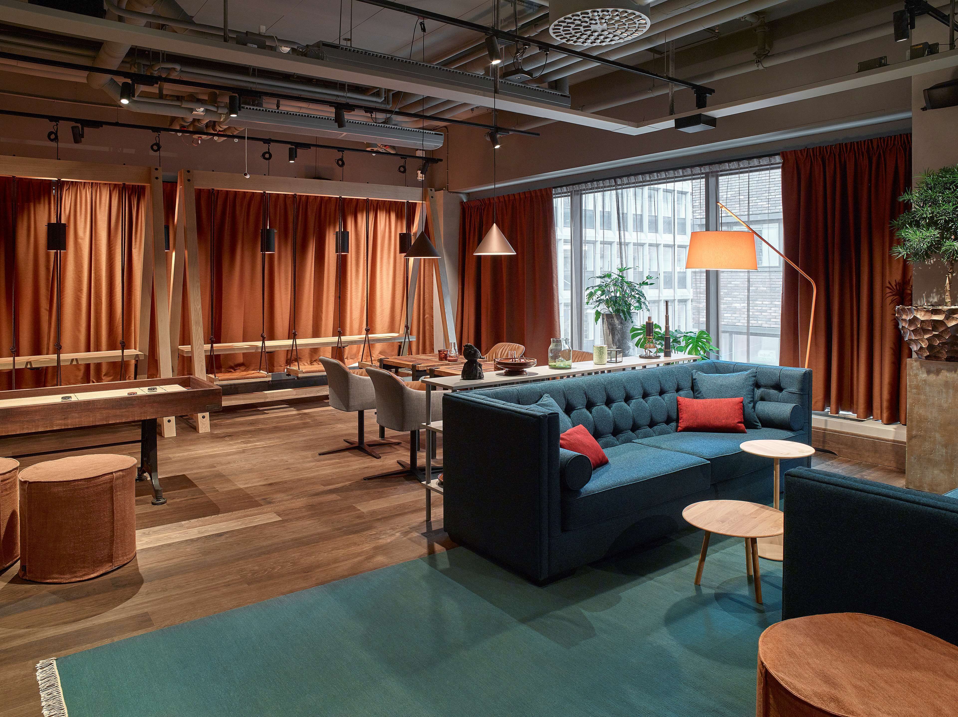 A modern interior with a blue sofa, wooden tables, and a large window with curtains.