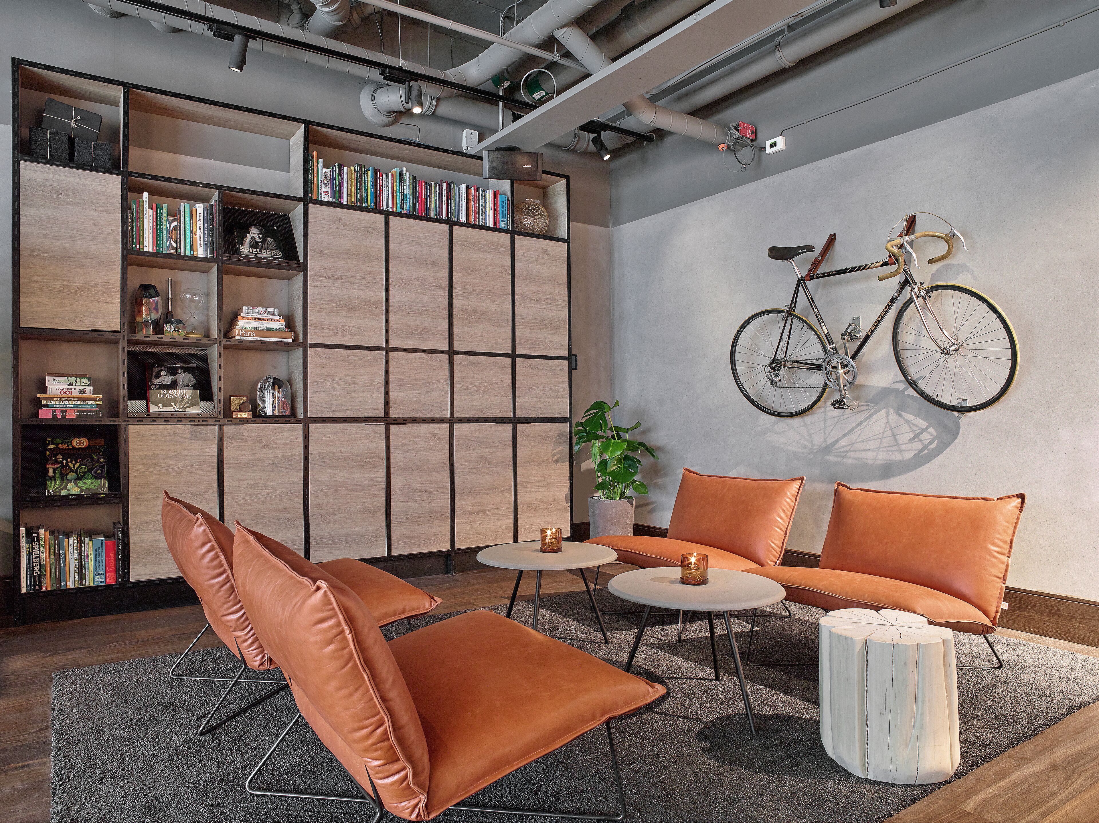 Una sala de estar moderna con una estantería, sillones de cuero, una mesa de centro redonda y una bicicleta colgada en la pared.