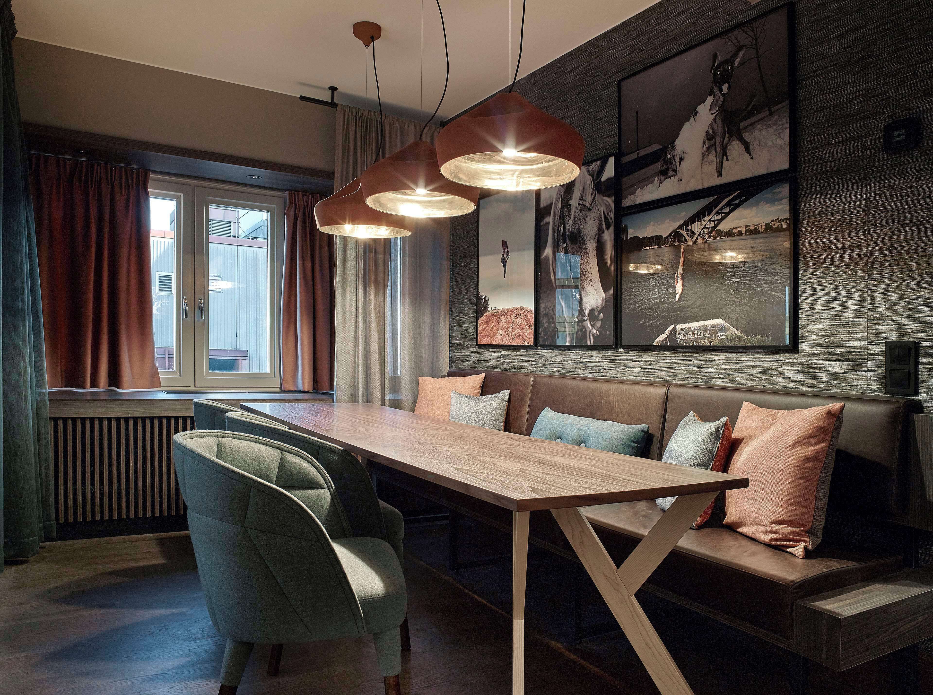 Un comedor moderno con mesa de madera, asientos acolchados, iluminación colgante y cuadros en la pared.