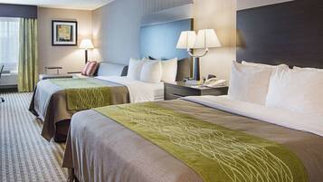 A hotel room with two beds, a desk, a chair, a lamp, and a painting on the wall.