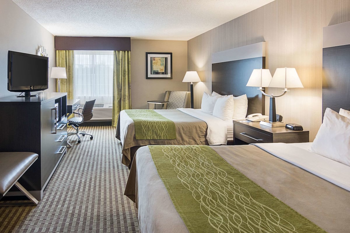 A hotel room with two beds, a desk, a TV, a chair, and a lamp.