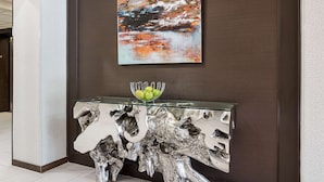 Un hall d’entrée moderne, avec une console dont le plateau est en verre, une sculpture métallique décorative et un grand tableau abstrait accroché au mur.
