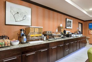A hotel breakfast area with a long counter, coffee machines, and a variety of food items.