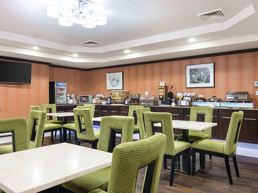 Un restaurante con sillas y mesas tapizadas de verde, una zona de bufé y un televisor de pantalla plana montado en la pared.