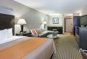Habitación de hotel con una cama grande, un sofá, una mesa de centro, un televisor y un área de kitchenette.