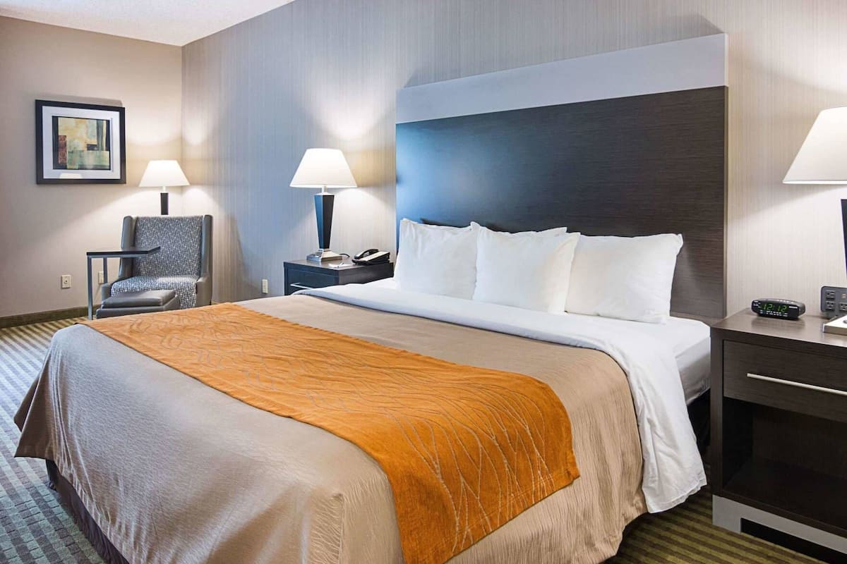 A hotel room with a bed, bedside tables, a chair, a lamp, and a clock.