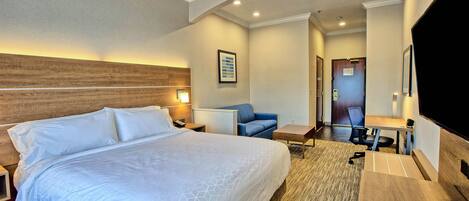 A hotel room with a large bed, a desk, a chair, a TV, and a door leading to another room.