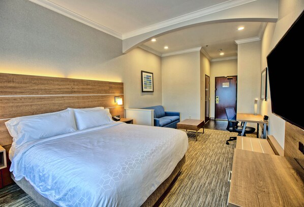 A hotel room with a large bed, a desk, a chair, a TV, and a door leading to another room. - Holiday Inn Express & Suites Davis - University Area by IHG (Davis)