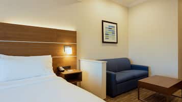 A hotel room with a bed, a nightstand with a phone, a blue armchair, and a small wooden table.