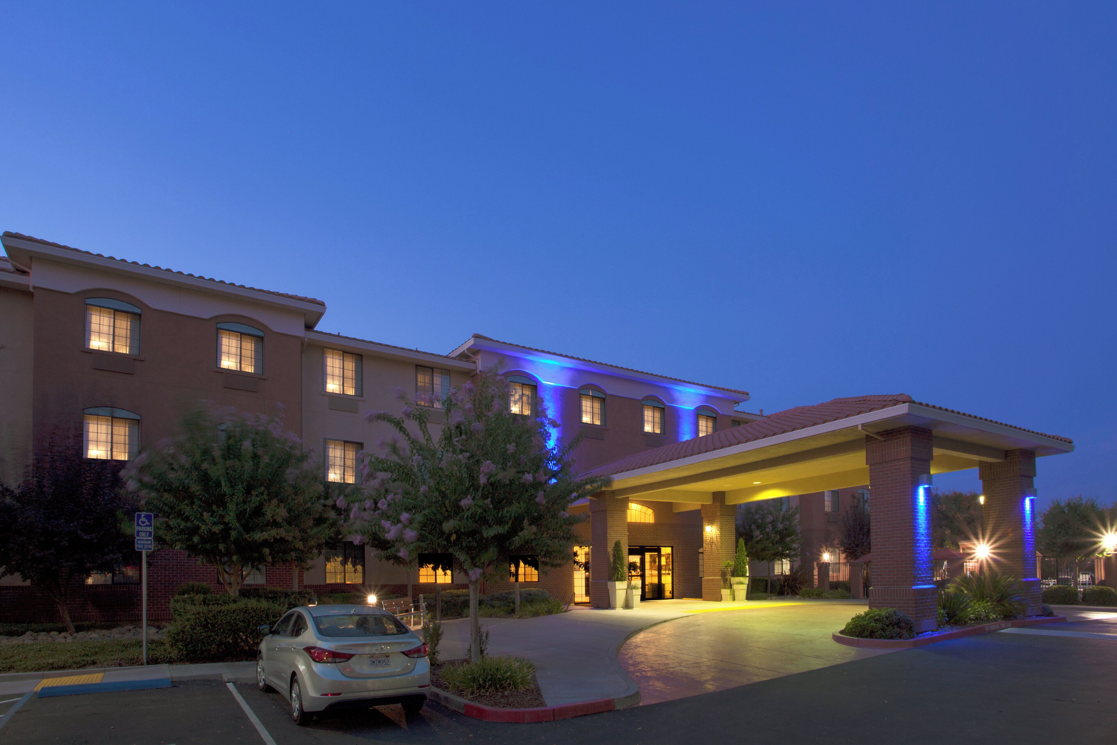 A hotel with a covered entrance, a parking lot, and a car parked in front.