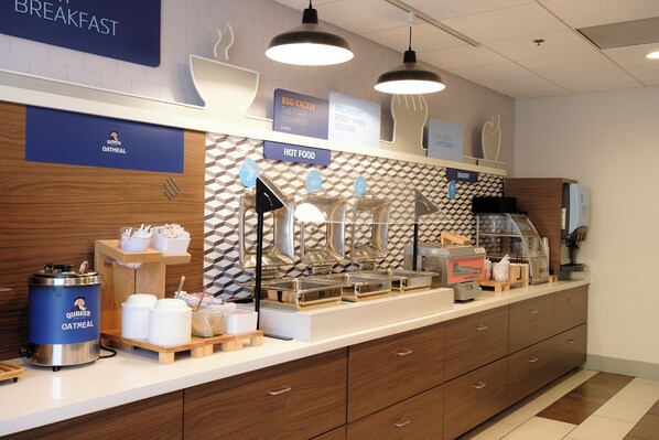 A breakfast buffet setup with various food stations, including a Quaker Oatmeal dispenser, and signs indicating breakfast options. - Holiday Inn Express & Suites Davis - University Area by IHG (Davis)