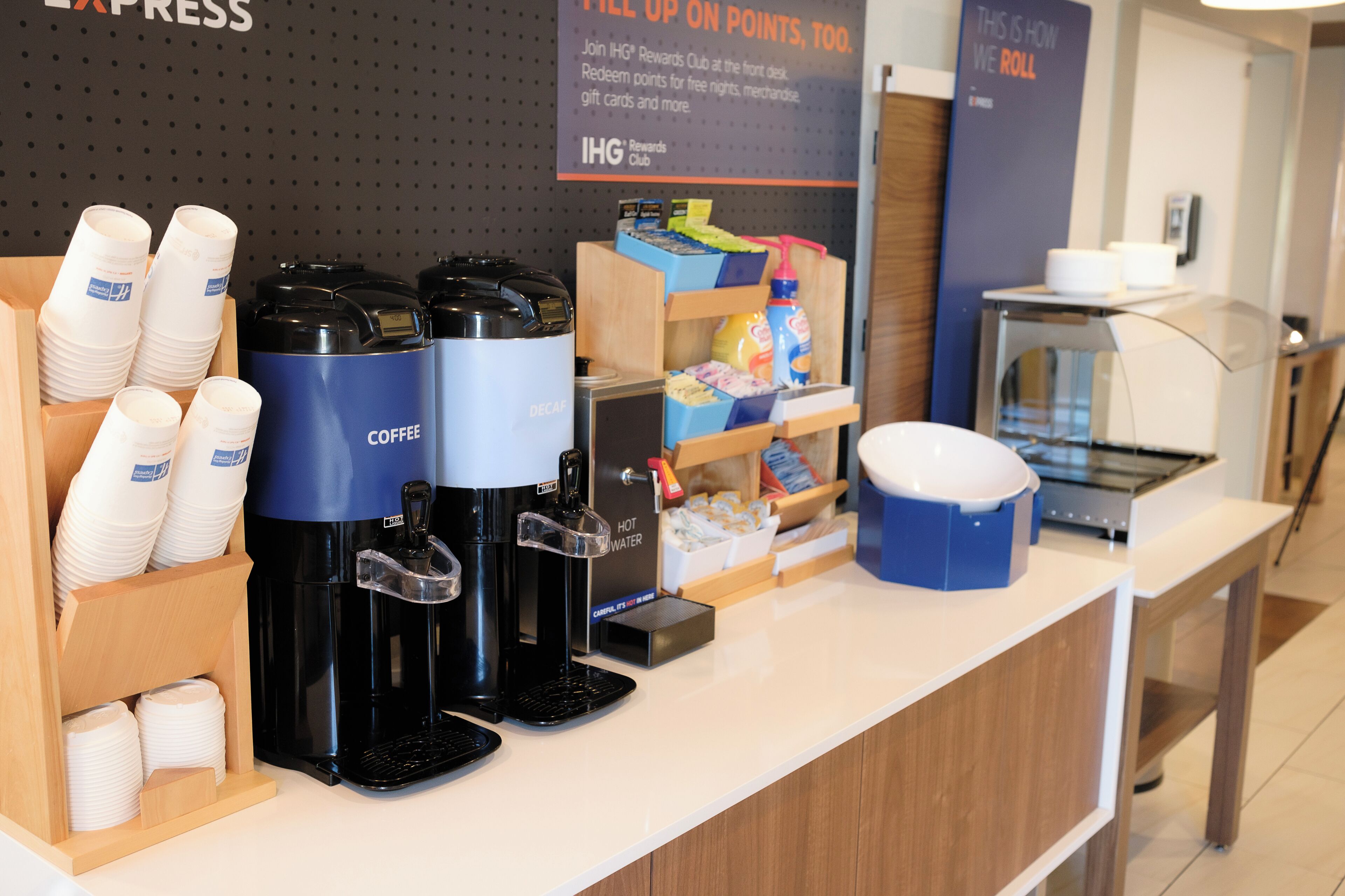 Una estación de café con varias máquinas de café, vasos desechables y un dispensador de agua.