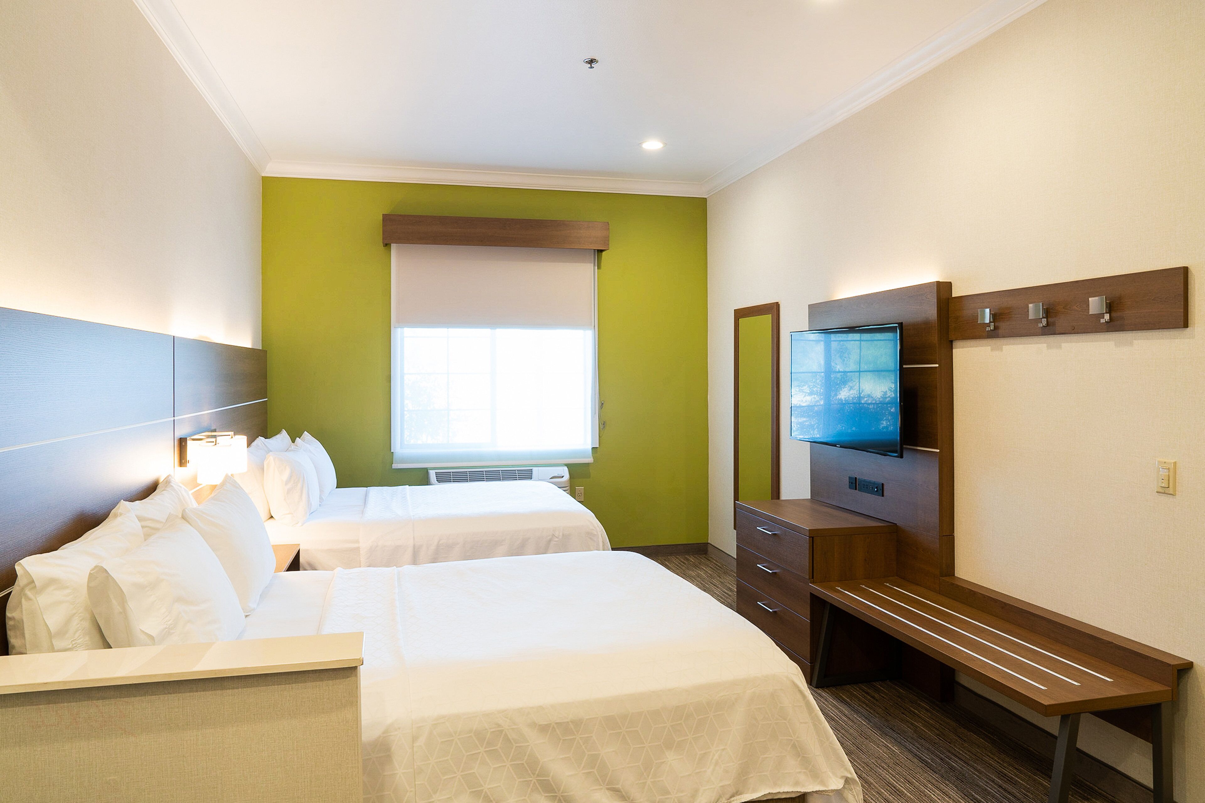 Habitación de hotel con dos camas, televisión, escritorio y ventana con persianas.