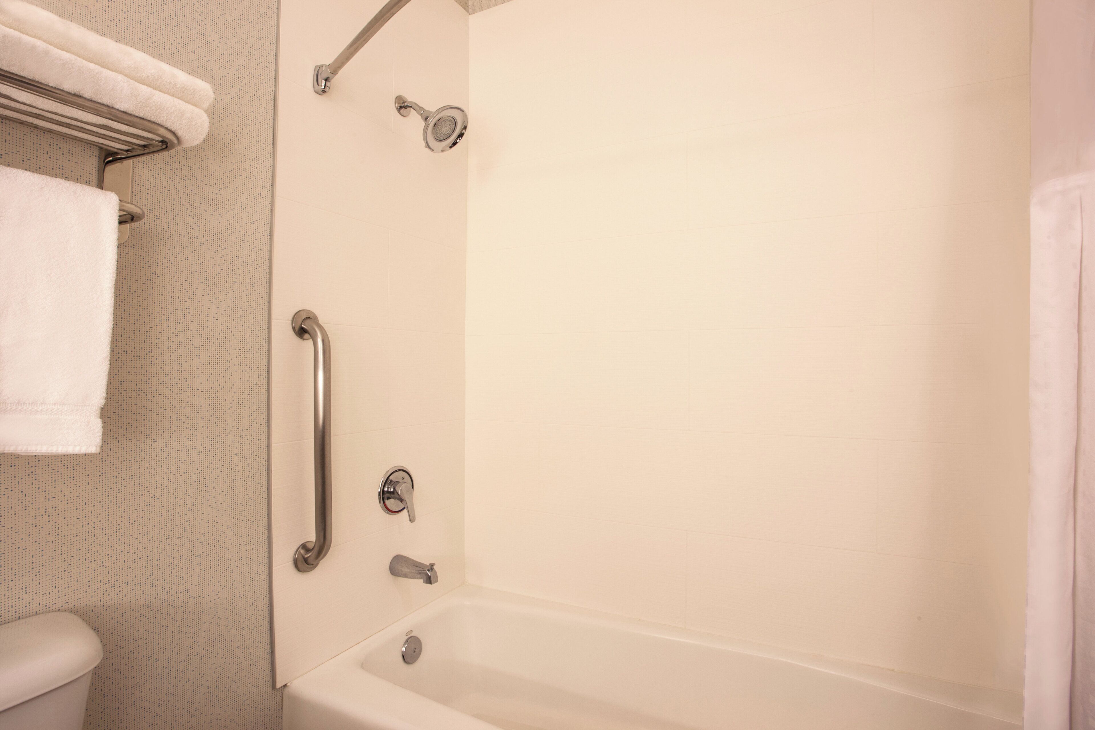 Een badkamer met een bad, een douche en een toilet. Er is een greep bevestigd in de buurt van de douche.