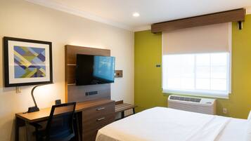 Habitación de hotel con cama, escritorio, silla, televisor y ventana con persianas.