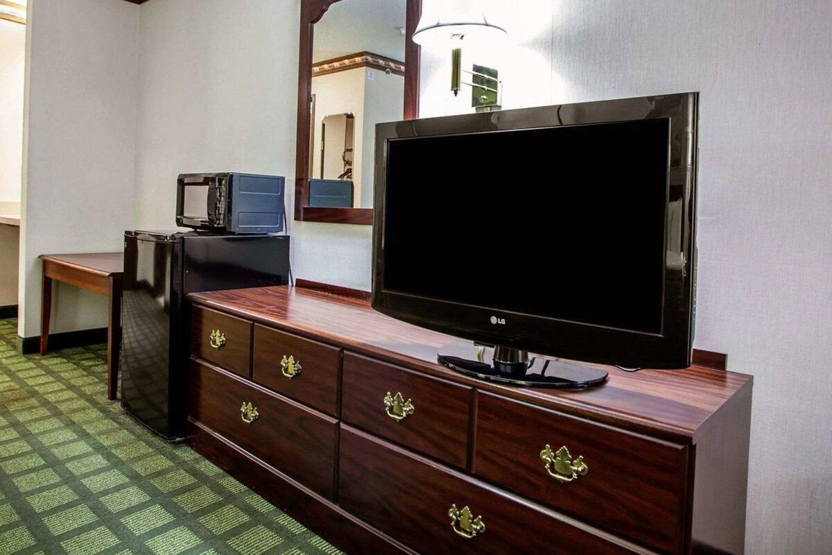 A hotel room with a wooden dresser, a flat-screen TV, a microwave, and a small table.