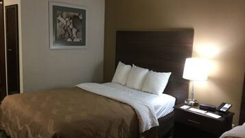 A hotel room with a bed, a nightstand with a lamp, a telephone, and a framed picture on the wall.