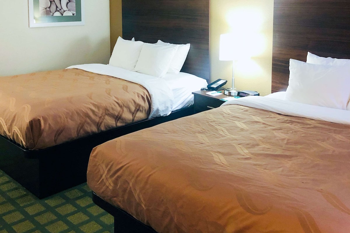 Two single beds with white linens, a nightstand with a lamp, and a framed picture on the wall.