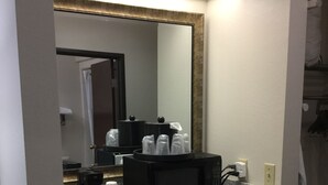 Une salle de bain d’hôtel avec un comptoir en granit, un micro-ondes noir, une machine à café et un miroir avec un cadre doré.