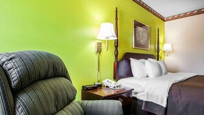 Une chambre d’hôtel avec un mur vert, un lit avec une literie blanche, une table de chevet en bois avec une lampe et un fauteuil à rayures.