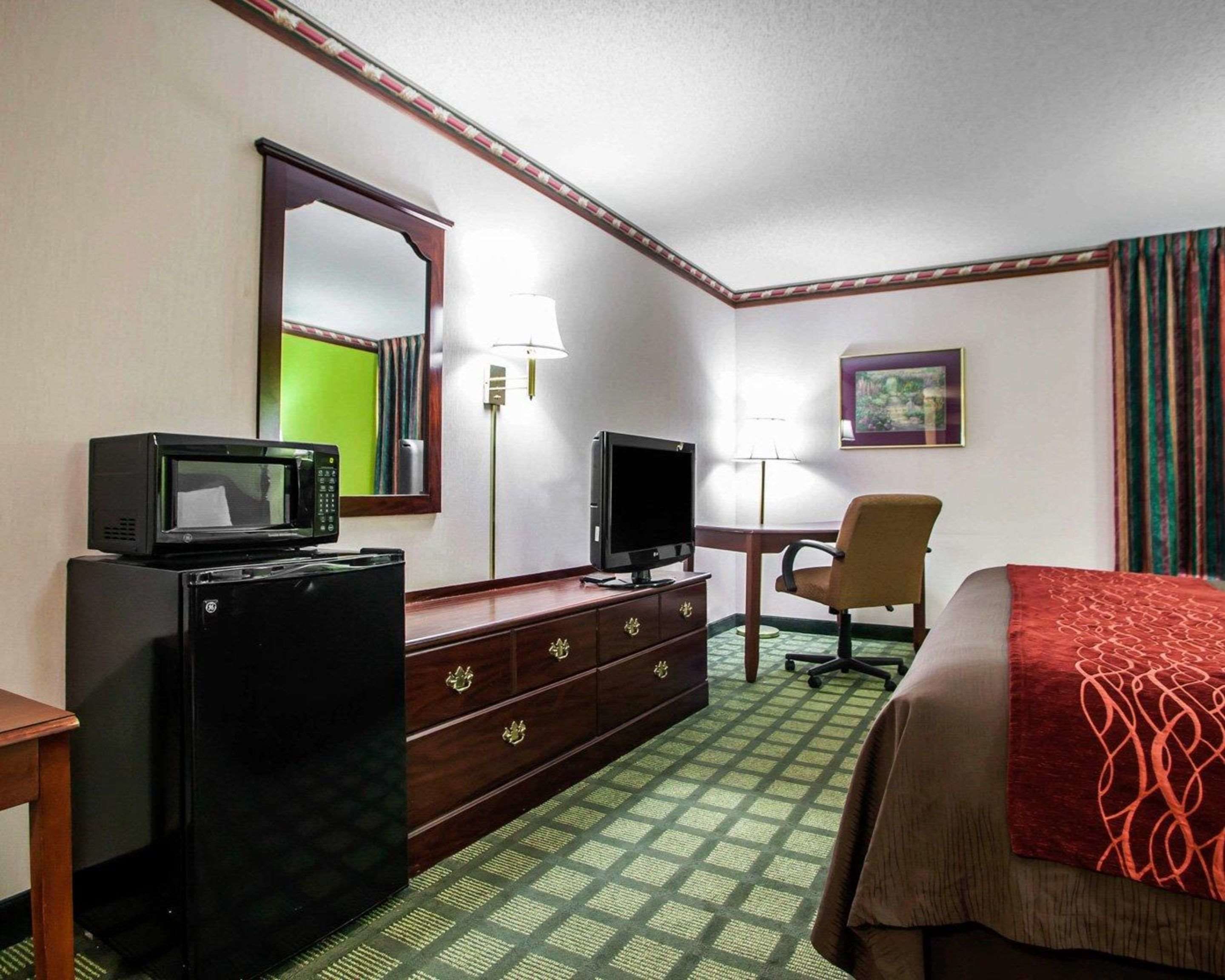 Ein Hotelzimmer mit Bett, Schreibtisch mit Stuhl, Fernseher, Mikrowelle und Kommode.