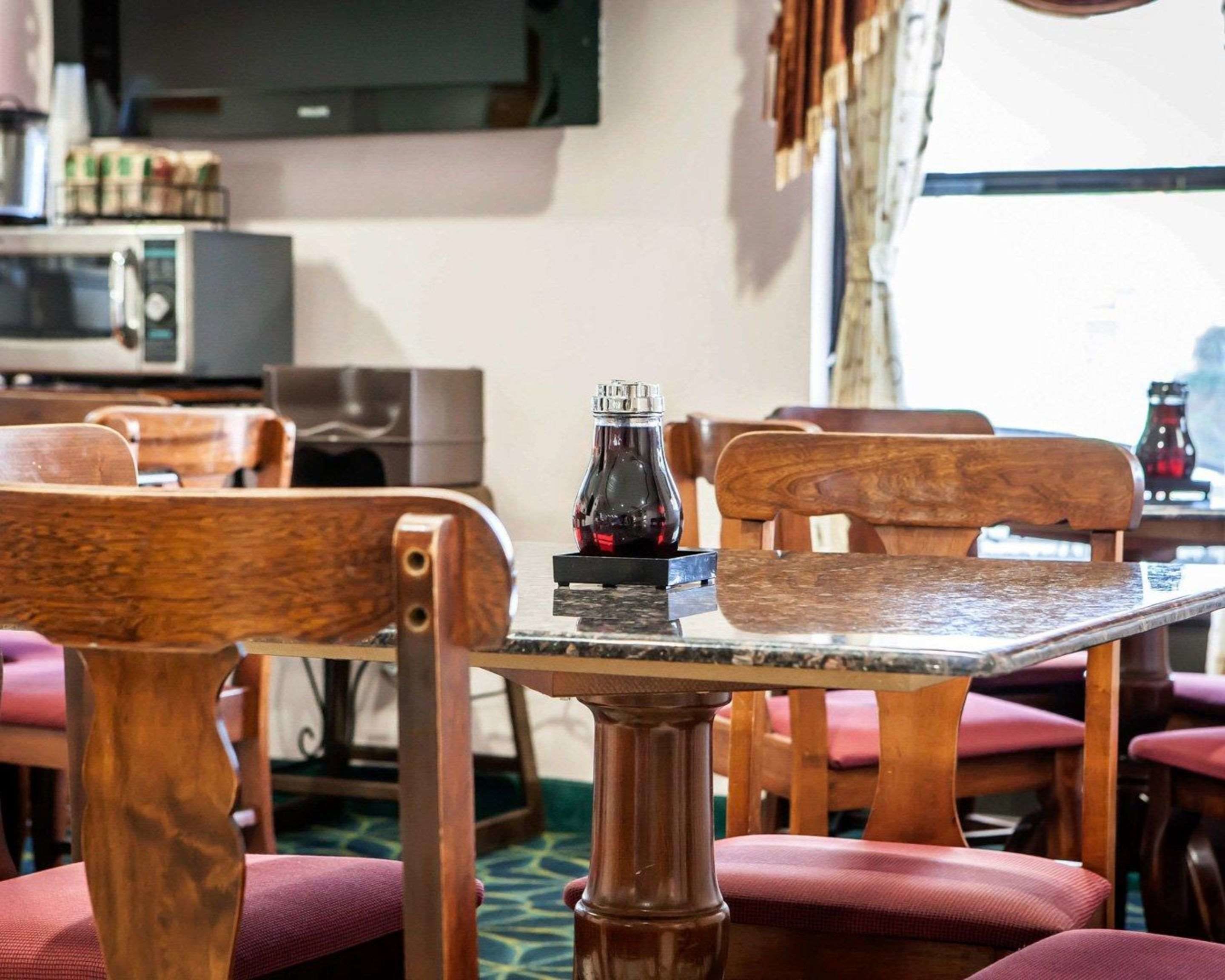 Un coin repas avec des chaises et une table en bois, une bouteille de boisson rouge et un four à micro-ondes en arrière-plan.