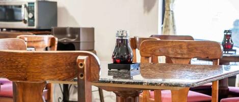 Un coin repas avec des chaises et une table en bois, une bouteille de boisson rouge et un four à micro-ondes en arrière-plan.