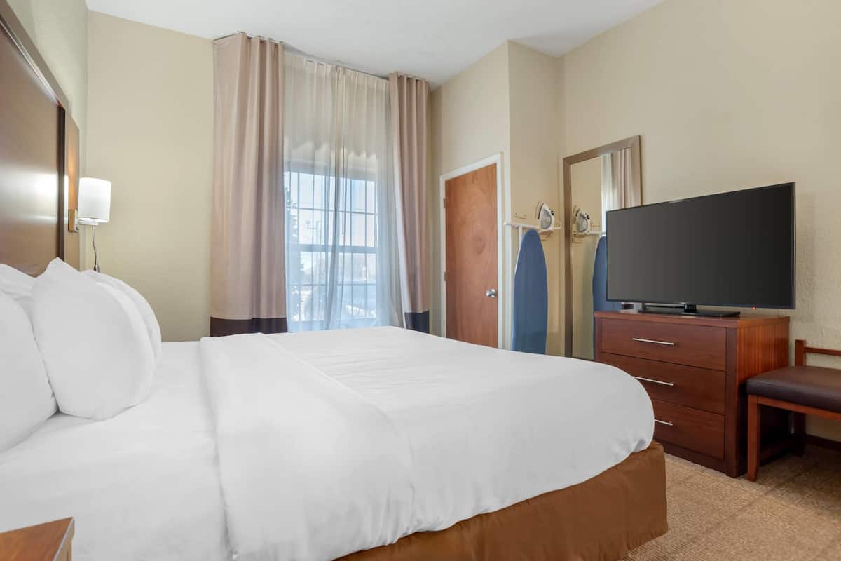 A hotel room with a large bed, a flat-screen TV, a wooden dresser, and a window with curtains.