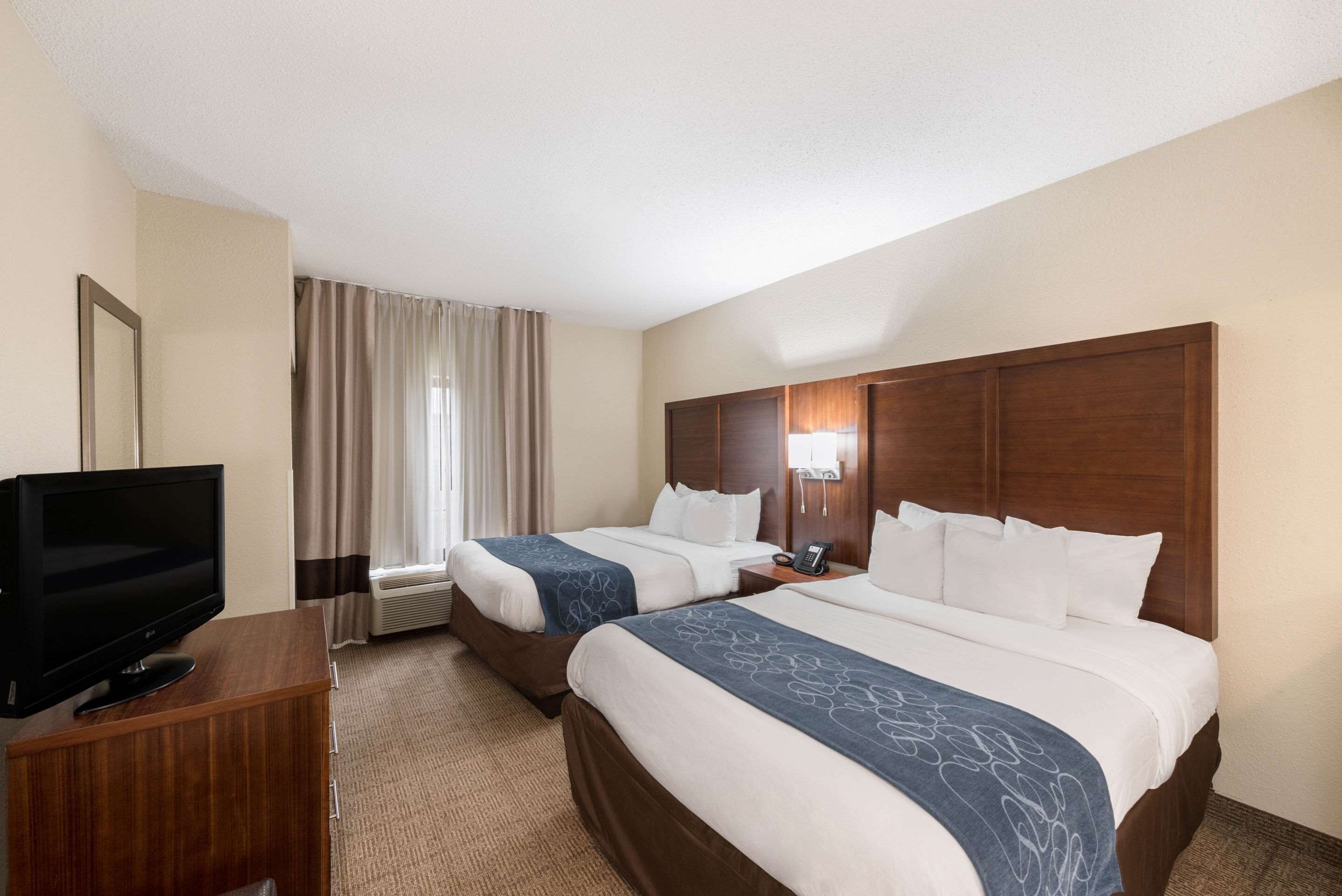 A hotel room with two beds, a TV, a desk, and a window with curtains.