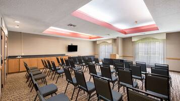 A conference room with rows of chairs, a podium, a flat-screen TV, and a carpeted floor.