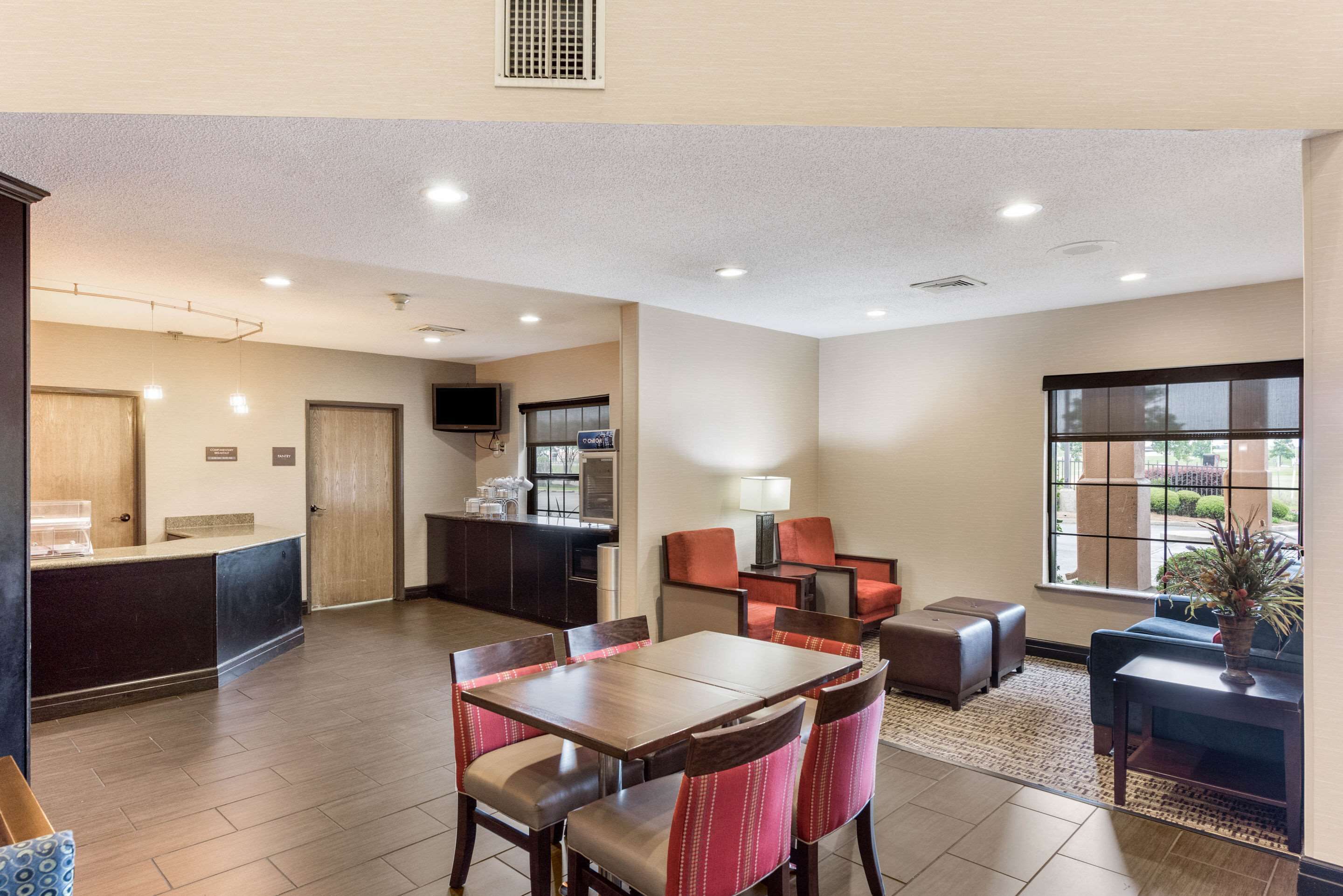 A hotel lobby with a reception desk, a dining area with a table and chairs, a kitchen area, and a large window with a view.