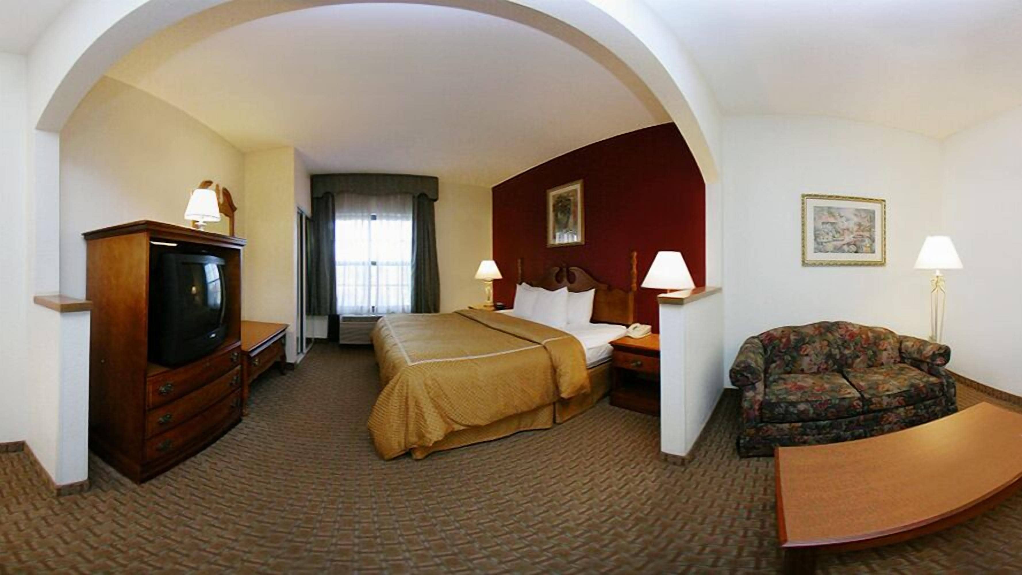 A hotel room with a bed, a television, a sofa, and a desk.