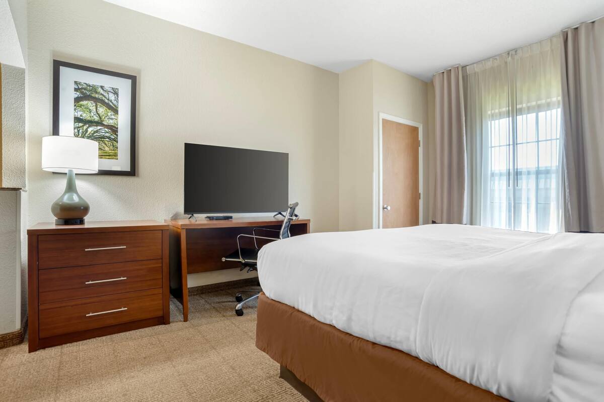 A hotel room with a bed, a desk with a computer, a lamp, and a framed picture on the wall.