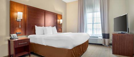Una habitación de hotel con una cama grande, cabecera de madera, lámparas de noche, un escritorio con teléfono, televisión y una ventana con cortinas.