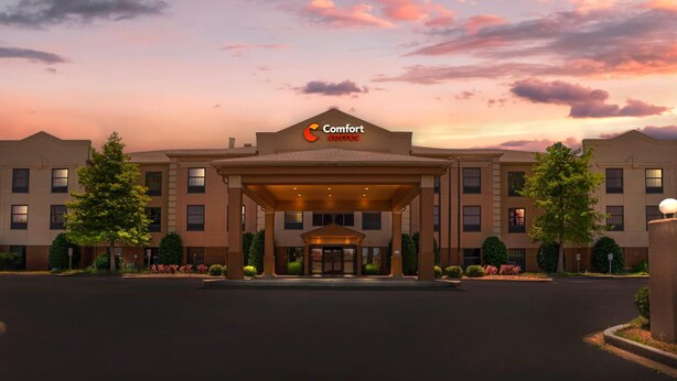 Um hotel Comfort Suites com entrada coberta, vários andares e um jardim frontal bem cuidado.