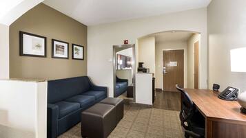 A hotel room with a sofa, a desk, and a kitchenette.
