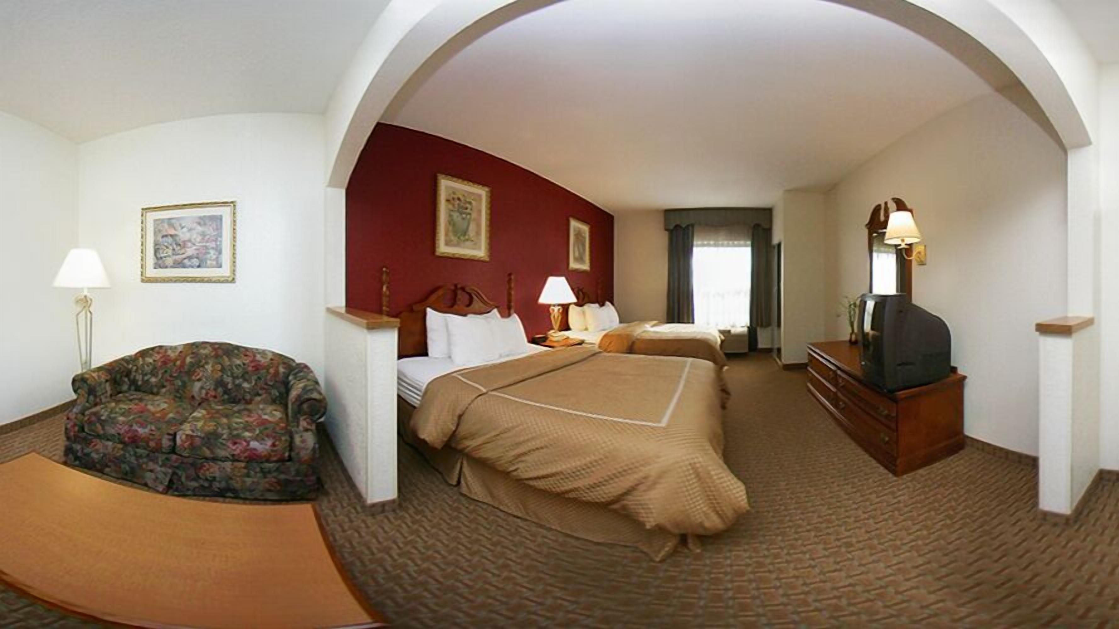 Una habitación de hotel con sofá, dos camas, televisión y chimenea.