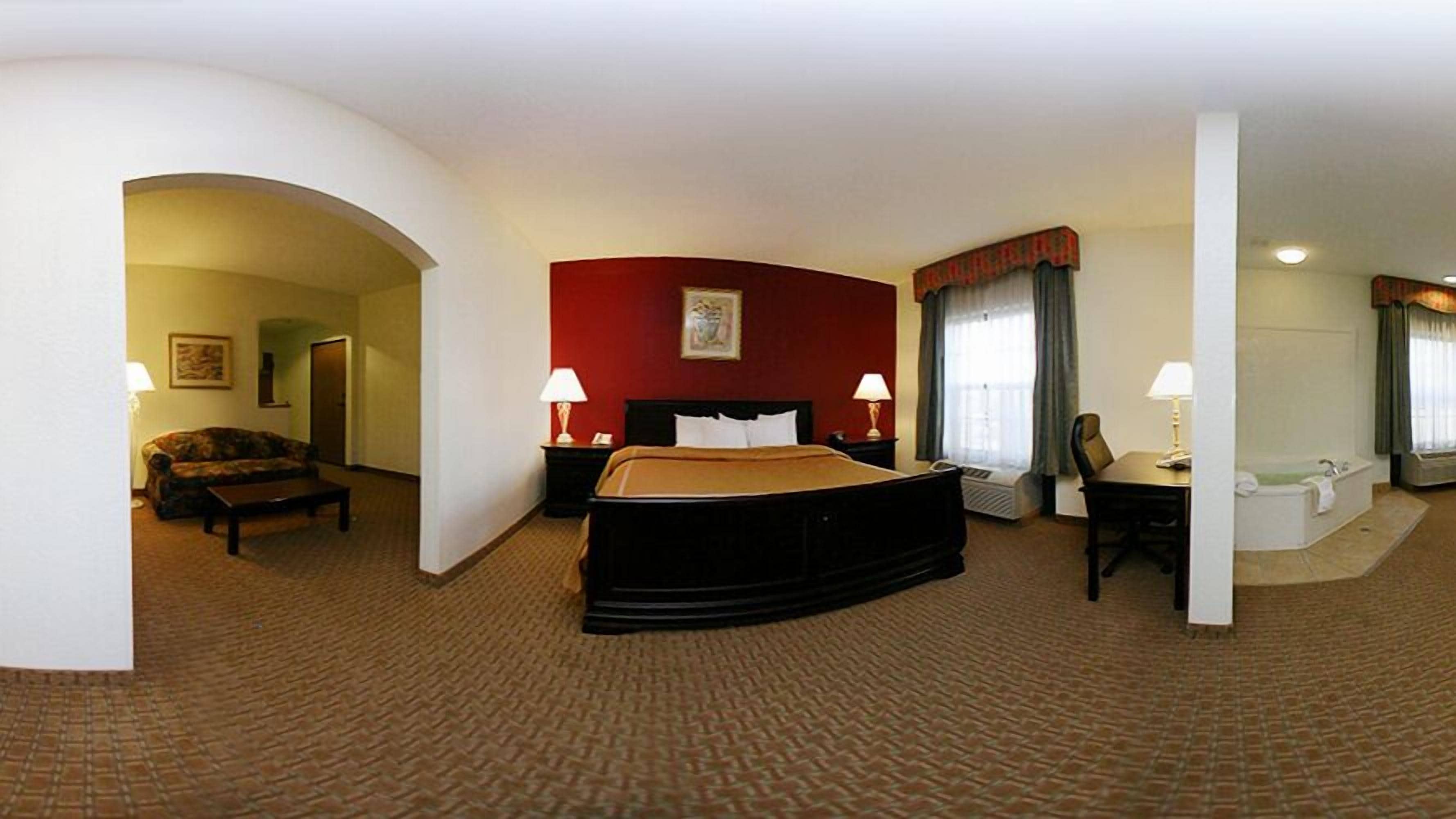 A hotel room with a bed, two bedside tables with lamps, a chair, a desk, and a bathroom with a bathtub.