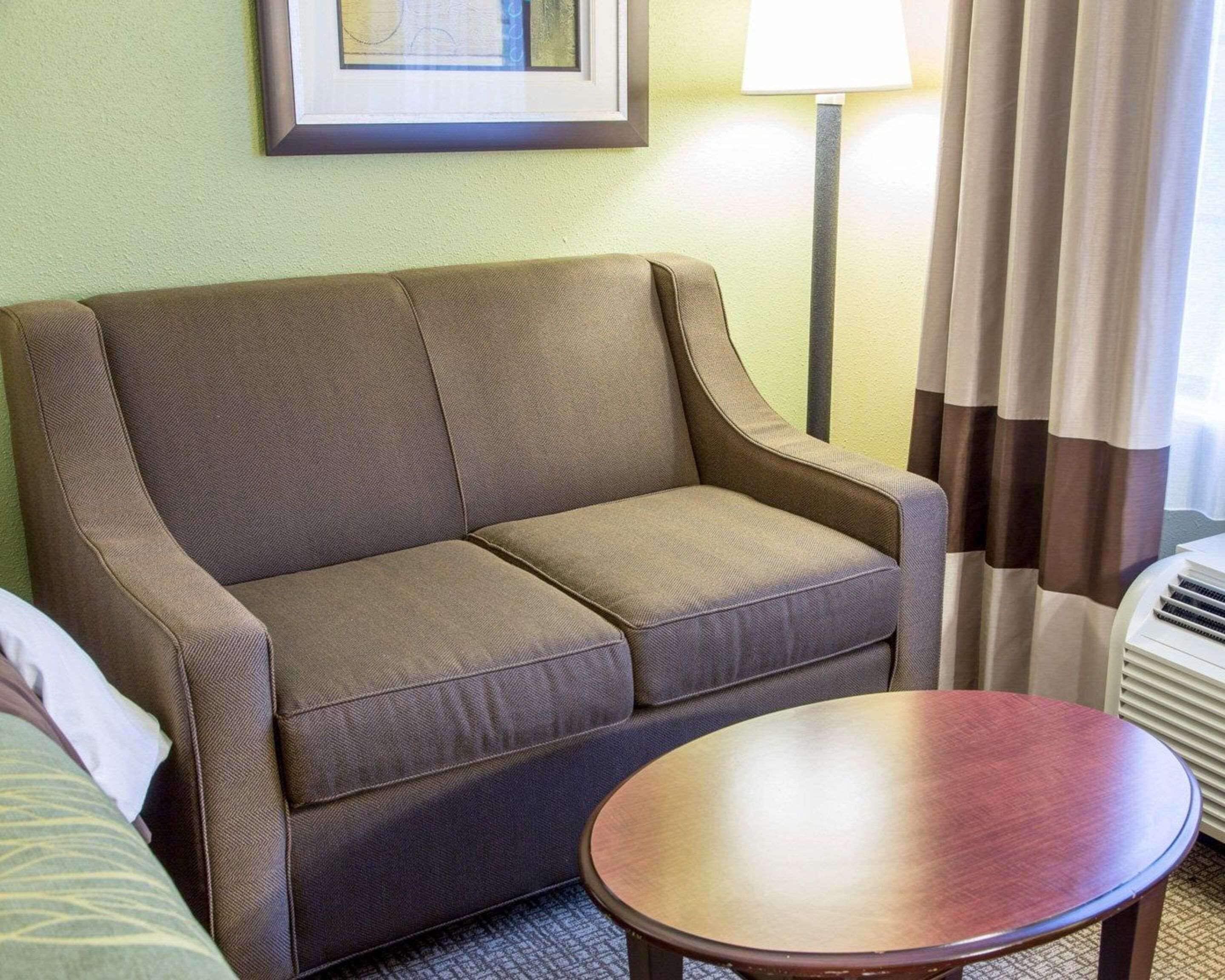 A brown sofa, a round wooden table, a lamp, and a window with curtains.