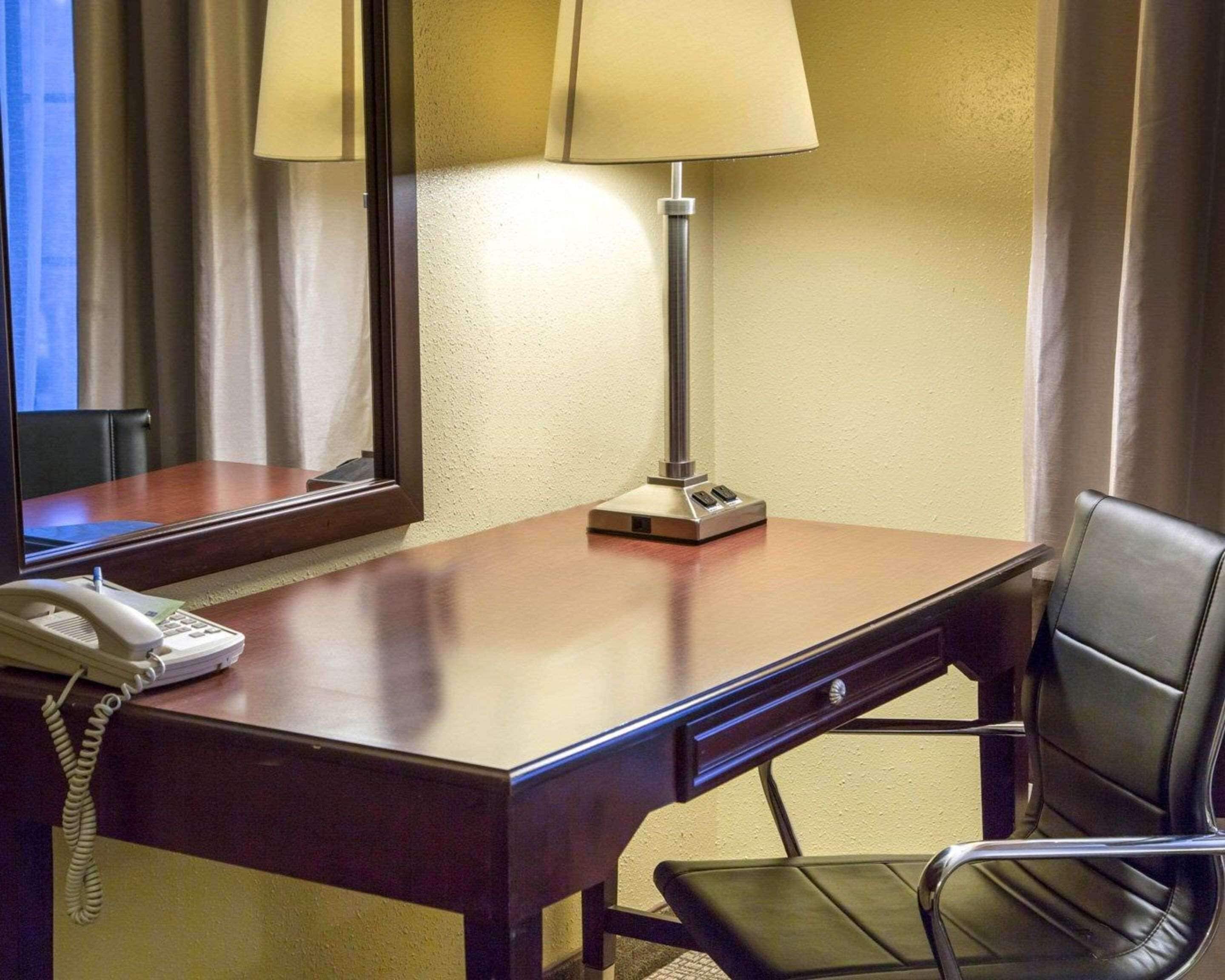 Habitación de hotel con un escritorio de madera, una lámpara, un teléfono y una silla.